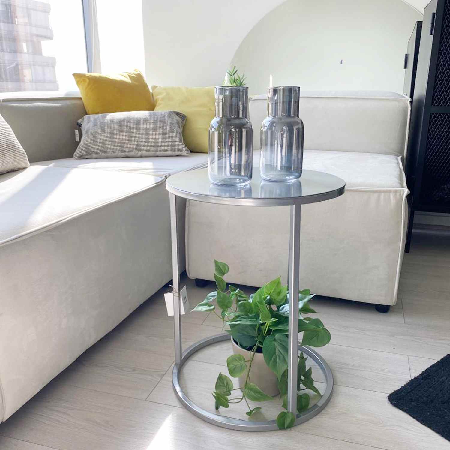 Mesa auxiliar metálica Nes Plata ambientada frente a un sofá